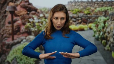 Huzurlu park ortamında tai-chi uygulayan bir kadın. Etrafı canlı yeşilliklerle çevrili. Gözleri kapalı.