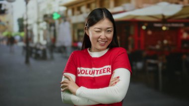 Şehir sokaklarında güvenle gülümseyen kırmızı gönüllü gömlekli, şehir arka planında bulanık bir kadın, modern Asyalı kimliğini ve açık havada toplum ruhunu yakalıyor..