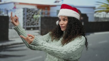Şehir sokağında kazak giymiş, açık havada anlamlı tavırları ve neşeli tavırlarıyla samimi bir anı yakalayan Noel Baba şapkalı bir kadın..
