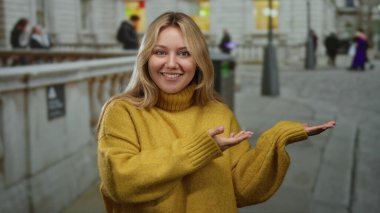 Sarı kazaklı kadın gülümsüyor ve elleri şehir sokaklarında, bulanık şehir geçmişiyle çevrili..