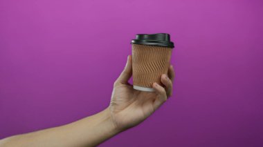 Kafkasyalı bir adamın elinde canlı mor arka planda kahve fincanı tutması, stüdyo ortamında soyutlanması, basitliği vurgulaması ve içecek kabına odaklanması..