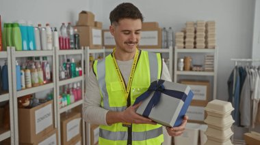 Yansıtıcı yelek giyen genç bir İspanyol, bağış merkezinde bir hediye kutusu tutuyor. Etrafında bir sürü malzeme var..