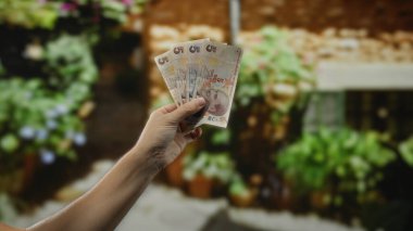 Adamın elinde Türk lira banknotları var. Şehrin bir caddesinde canlı bir şehir ortamında, bulanık çiçekli bir arka planda yerel para sergiliyor..