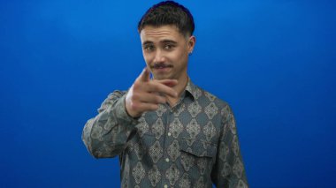 Genç adam kendine güvenen bir tişörtle izole edilmiş mavi bir arkaplanı işaret ederek dikkatleri üzerine çekiyor ve nişan alıyor..