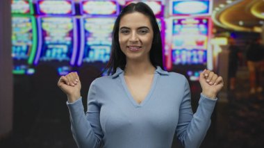 Canlı bir kumarhanede arka planda neon kumar makineleriyle gülümseyen bir kadın neşeli bir ifade ve kutlama sergiliyor. Canlı bir oyun atmosferinde heyecan ve şans yakalıyor..