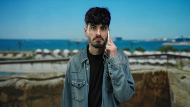 Manzaralı deniz kıyısında, arka planda okyanus manzaralı akıllı telefondan konuşan bir adam günlük şehir yaşam tarzını sergiliyor..