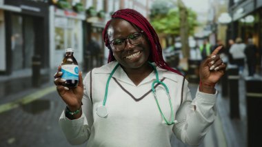 Sokakta gülümseyen bir kadın elinde steteskopla ilaç şişesiyle, açık havada sağlık bilincini ve şehir yaşam tarzını ön plana çıkarıyor..