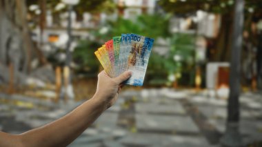 Şehir caddesinde renkli İsviçre frangına sahip bir adam, açık şehir ortamında paraların altını çiziyor, arka planı bulanık, İsviçre 'de finansal temalar sergiliyor..