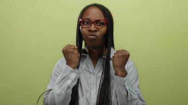 Gözlüklü ve uzun örgülü bir kadın sarı bir arka plana karşı duruyor hayal kırıklığına uğramış görünüyor, öfke ve kararlılık duygularını iletiyor..