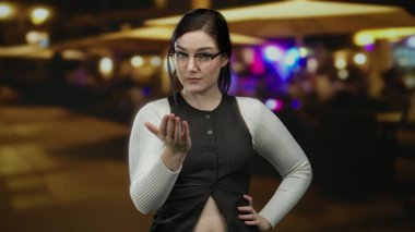 Gece canlı bir terasta gözlüklü gülümseyen bir kadın. Bulanık restoran ışıklarıyla sıcak bir sokak havası yaratıyor..