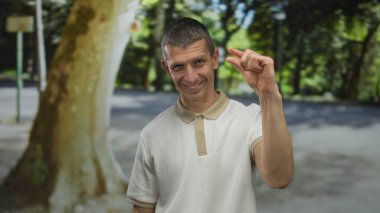 Dışarıdaki adam, arka planda bulanık ağaçlar ve kırmızı otobüsle sokakta gülümseyen küçük parmakları olan jestler yapıyor..