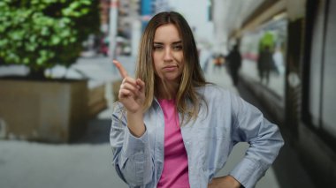 Şehir sokaklarında jest yapan, arka planda bulanık giysiler giyen şehir ortamında el işaretleriyle duygularını ifade eden genç bir kadın..