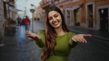 Genç İspanyol kadın açık bir caddede davetkar bir şekilde gülümsüyor açık bir şehir ortamında neşeli bir ifade sergiliyor neşeli bir şehir havası yakalıyor..