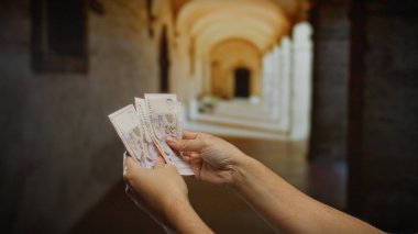 Üniversite koridorunda tek kişilik dolarları tutan eller, döviz kuru dinamiklerine odaklanarak iş, finans ve kapalı alandaki yatırımları vurguluyor..