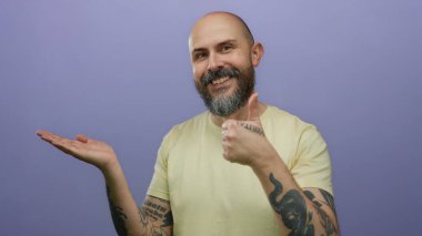 Dövmeleri olan beyaz sakallı bir adam, izole edilmiş mor bir arka plana gülümserken elini açacağını gösteriyor.