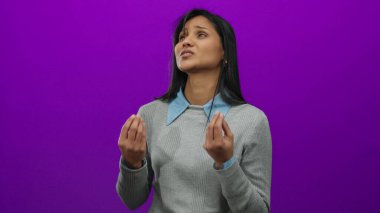 Gri bir süveter ve mavi yakalı gömleği olan canlı mor bir arka plana karşı hareketli bir kadın katı bir arkaplanda duygularını ve tarzını gösteriyor..