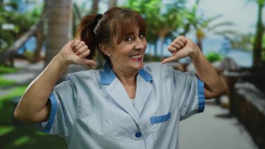 Üniformalı, kıdemli, gülümseyen bir kadın, açık hava parkı ortamında, mesleğinin gururunu ve neşesini gösteriyor..