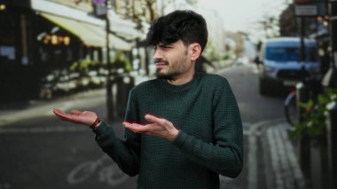 Kentsel caddelerde omuz silken bir adam, şehir ortamında gündelik tarz ve eğlence ifadesiyle ayakta dururken kargaşa ya da belirsizlik taşır.