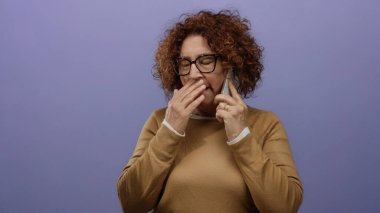 Esmer, orta yaşlı, İspanyol bir kadın, izole edilmiş mor bir duvara karşı, gözlük takıyor, düşünceli ve sıradan görünüyor..