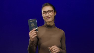 Birleşik Devletler pasaportu taşıyan genç bir kadın canlı mavi arka planda güvenli bir şekilde izole edilmiş şekilde gülümsüyor..