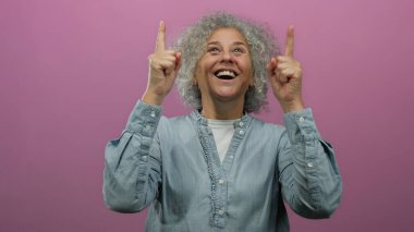 Gülümseyen, parlak pembe arka plana işaret eden, neşe ve pozitif enerji gösteren bir kadın..