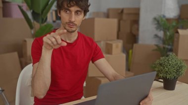 Adam bir binanın karton kutularıyla çevrili bir masadaki dizüstü bilgisayarı işaret ediyor; verimlilik.