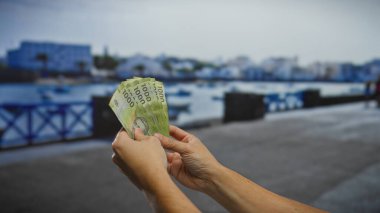 Şili pesolarını sahil caddesinde tutan adam, manzaralı bir liman şehrine yatırım ya da alım satım yaptığını gösteriyor..