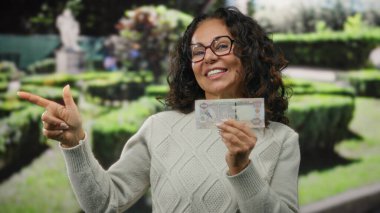 Parkta orta yaşlı bir kadın elinde Uae Dirham banknotu tutarken heyecanla işaret ediyor..