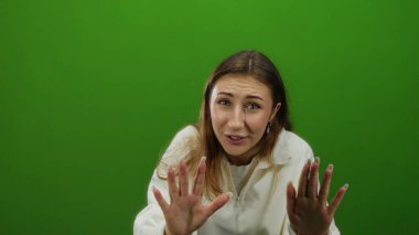 İzole edilmiş yeşil bir arka plan duvarına karşı el kol hareketi yapan bir kadın, heyecan verici bir video çerçevesinde duygu ve yüz hareketleriyle ifade ediyor..