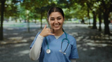 Steteskop ve neşeli bir ifadeyle hemşire gibi giyinmiş bir kadın açık hava parkında jest yapıyor..
