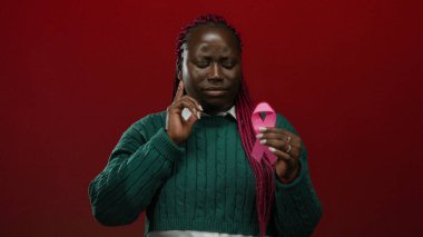 Elinde pembe kurdele tutan kadın canlı kırmızı arka plan göğüs kanseri farkındalığını sembolize ediyor..