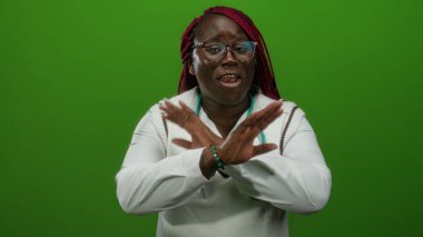 Gözlüklü ve steteskoplu kadın yeşil arka planda el hareketleriyle gülümsüyor, beyaz giyiniyor, enerji ve iletişim taşıyor, izole ortama karşı.