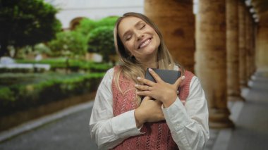 Bir kadın gülümsüyor ve bir kitabı kucaklıyor şehir sokaklarında dikilirken, şehir ortamında neşeli hissederken..