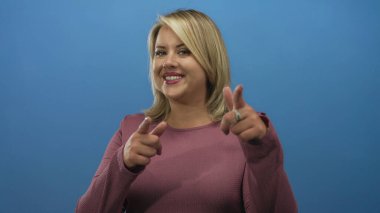 Mavi stüdyoda genç sarışın bir kadın işaret ediyor ve gülümsüyor. Güven motivasyon başarısı..