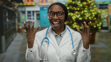 Kadın doktor gözlüklü ve steteskop takmış gülümsüyor. Şehir sokağında şenlikli ışıklar ve binalarla dikiliyor..