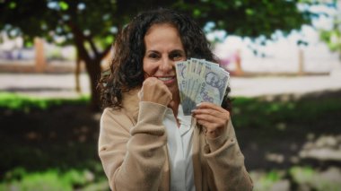 Orta yaşlı bir kadın parkta heyecanla Romanya banknotlarını tutuyor. Açık havada mali başarıya işaret ediyor..