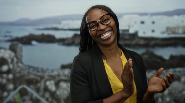 Sahilde deniz kenarında dalgalı saçlarıyla gülümseyen kadın manzaralı deniz manzaralı ve arka planda binaları olan.