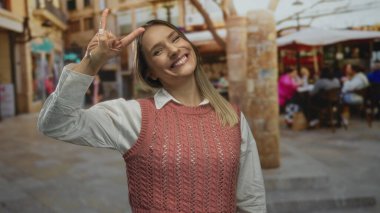 Şehir terasında gülümseyen bir kadın. Arka planda insanlar var. Lokantada kahvenin tadını çıkarıyorlar..