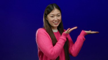 Mavi arka planda poz veren, pembe süveter giyen, gülümseyen ve anlamlı, canlı bir karakteri tek başına yakalayan bir kadın..