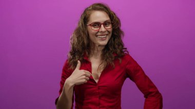 Kırmızı gözlüklü ve tişörtlü canlı pembe bir arka plana güvenerek gülümseyen bir kadın..