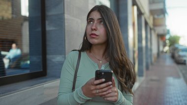 Şehirdeki sokak ortamında akıllı telefon kullanan bir kadın şehir yaşamının ortasında cep telefonuyla meşgul olan düşünceli, genç bir İspanyol kadını sergiliyor..