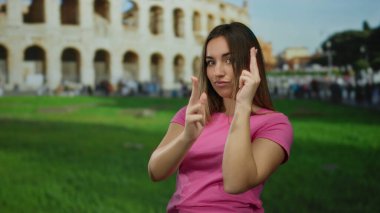 Pembe gömlekli kadın Roma 'daki sembolik Roma kolezyumunun yanında el hareketi yapıyor. Açık havada eğlenceli ve tarihi mimariyi yeşil çimlerle harmanlıyor.