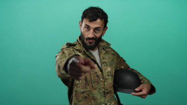 Sakallı İspanyol üniformalı adam yeşil arka planda ileriye bakan miğfer tutuyor..