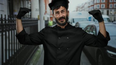 Sakallı İspanyol erkek aşçı hareketleriyle kalabalık bir caddede siyah giyinmiş ve eldiven giymiş arka planda araçlarla açık havada aşçılık tutkusu sergiliyor..