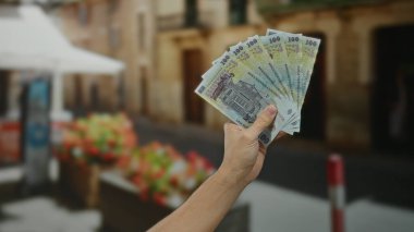 Bir kentin arka planında Romen banknotlarını tutarak, hareketli bir günde beyaz bir erkekle açık hava finans veya ekonomi konseptini öneriyor..