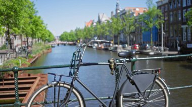 Bokeh arka planında ağaçlar ve evler olan köprü üzerindeki bisiklet Hollanda şehir hayatının özünü yakalıyor..