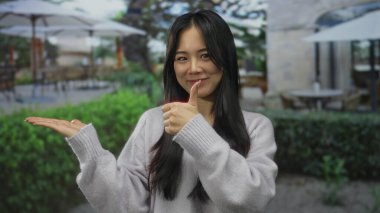 Yeşil bahçeli ve terasta şemsiyeyle kaplı masaları olan açık hava restoranında gülümseyen Çinli bir kadın..