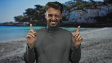 Parlak güneş altındaki kayalık sahil kayalıklarının yakınındaki kumsalda yüzünü buruşturan ve işaret eden adam hayal kırıklığı.