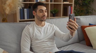 İspanyol bir adam rahat bir oturma odasında akıllı telefonunu kullanarak ev ortamında rahat ve rahat bir atmosfer yaratıyor..