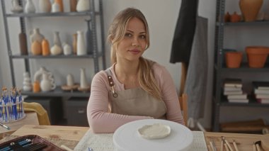 Kadın seramik stüdyosundaki dönen çarkın üzerinde çömlek aletleri ile kaplı kil diski şekillendiriyor; yaratıcılık odaklı konsantrasyon.